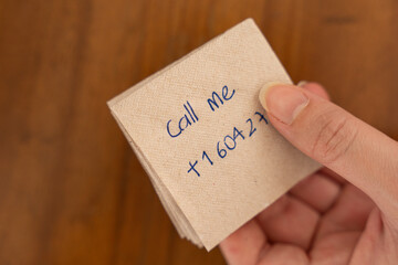 Human Connection: Offering a Phone Number.
Hands deliver a message on a napkin placed on a wooden...