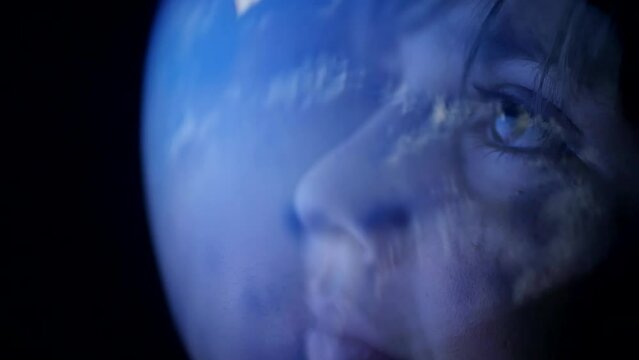 A boy in a spacesuit helmet watches the blue planet earth from outer space. The child dreams of exploring the galaxy and planets. Adventures in zero gravity and flight to the stars