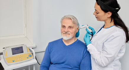 Experienced audiologist with tympanometer probe doing tympanometry procedure and impedance audiometry for senior male patient at audiology center