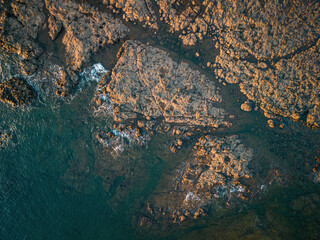 Top-down view of rocks getting washed by waves in the sunset shining orange light
