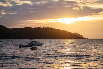 Golden hour sunset view of beach with boat on water and island in pacific ocean