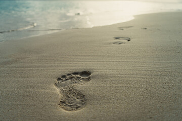  Low angle footsteps in white sand on beach and shore in background at golden hour