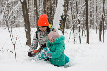 Fototapeta na wymiar Mom and daughter are playing in the snow and making a snowman. Winter walk in the fores