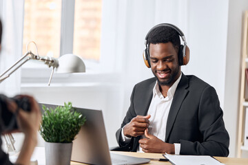 An African-American man sits at his desk in front of his laptop, wearing headphones and chatting on a video call, listening to music. The concept of student business training and online work.