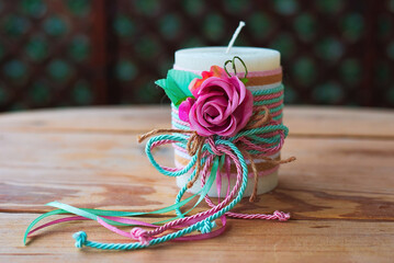 decorative white candle, with a rose and ribbons, on a wooden table.