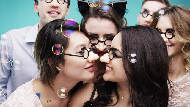 Happy people, bubbles and party with glasses, celebration and eskimo kiss with friends. Dancing, photobooth and bonding together with men, woman and social gathering on studio background for fun