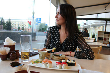 A beautiful girl is sitting in a cafe and eating Japanese sushi