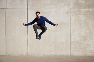 Joyful, ecstatic adult man jumping agains concrete wall - obrazy, fototapety, plakaty