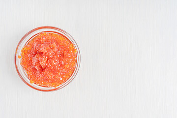Top view of red salted salmon caviar or fish roe served in glass bowl on white wooden background...