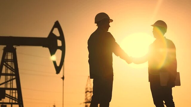 oil business. workers of the fuel industry shaking hands with oil pumps on the background. industry business oil and gas concept. engineers of the station handshake silhouette at lifestyle sunset