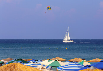 Multi-colored beach umbrellas against the background of a blue sea sky and a yacht.