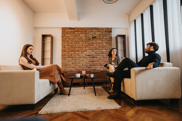 Three adults engaged in a relaxed conversation in a cozy living room with brick wall accents and modern decor.