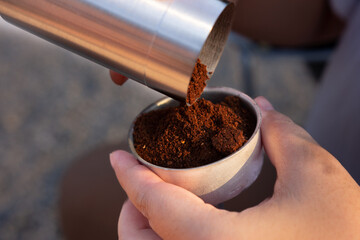 Aromatic roasted coffee beans fill a coffee powder container held in a hand, creating a close-up...