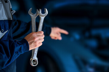 Auto mechanic working show on car broken engine in mechanics service or garage. Showing thumb up gesture while standing with auto mechanic with wrench in hand near broken car in garage.