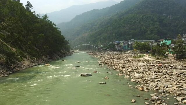 Aerial view above the Tista river, in a valley between mountains and Indian forest, on a sunny day, in Sikkim, India.