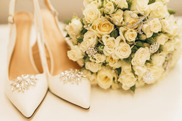 Beautiful bridal fashionable wedding white high heels shoes,  and a bridal bouquet on a desk at home.  Wedding