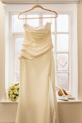 Beautiful bridal fashionable wedding white high heels shoes, dress, and a bridal bouquet near a window at home.  Wedding