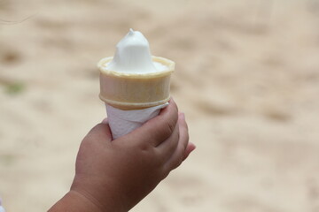 Ice cream cone in child hand on sand background, soft focus.