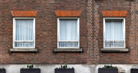 three aligned classic white windows of typical london architecture with red brick wall