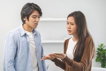 Infidelity, suspicion asian young couple love fight relationship, wife holding cellphone, smartphone cheating on phone, scolding husband about mistrust, distrust and jealousy at home.