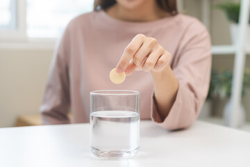 Smile asian young woman putting or dropping effervescent tablet into glass of water, holding pain...