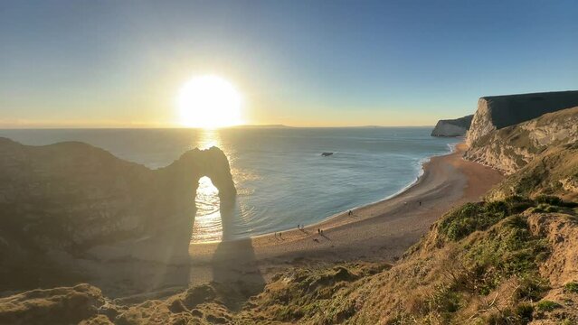 The sun goes down on the Jurassic coast and Durdle Door in Dorset with Seak Pink Trift growing on the top of the cliff in the foreground. Durdle Door, Dorset, Jurassic Coast, England, UK