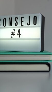 Horizontal. Letrero retro-iluminado con el texto "Consejo 4" sobre dos cuadernos uno negro y otro turquesa sobre mesa y fondo blanco. Terminando la vista sobre un bote de bol&iacute;grafos. Concepto ideas