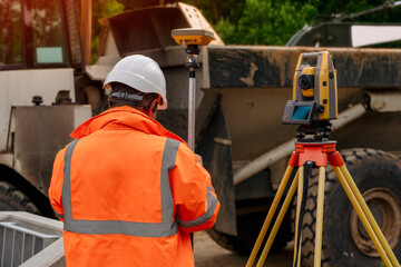 Surveyor site engineer with total positioning station on the construction site of the new road construction with construction machinery and materials  in the background