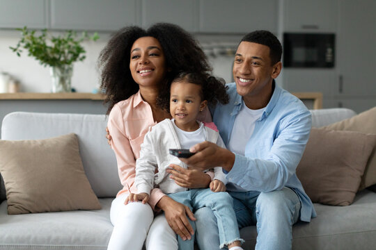 Happy Black Family Of Three Watching Tv At Home, Parents And Cute Little Daughter Resting On Couch In Living Room, Free Space