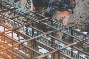 A worker uses steel tying wire to fasten steel rods to reinforcement bars close-up. Reinforced...