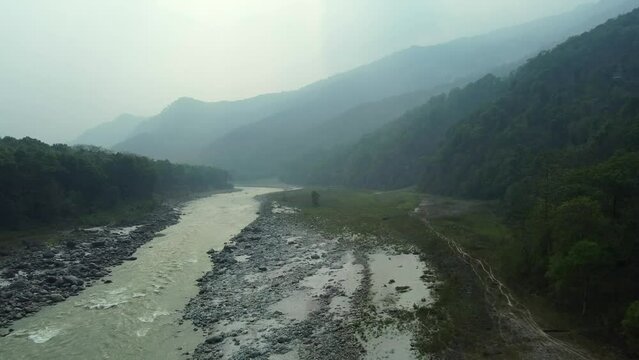 Aerial view above the Tista river, in a valley between mountains and Indian forest, on a sunny day, in Sikkim, India.