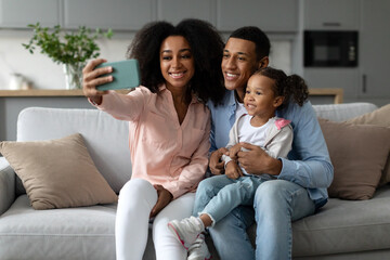 Happy african american family taking selfie together at home, parents posing with their daughter...