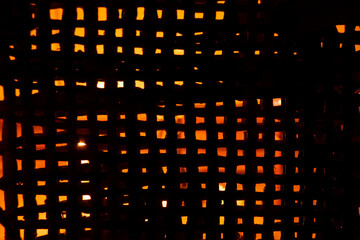 The light of a candle is visible through a fine straw mesh in the dark, background, mesh