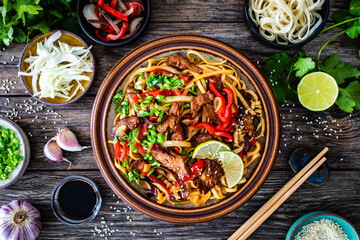 Asian style stir fried vegetables, roast beef and chow mein noodles on wooden table
