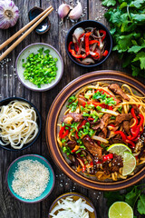Asian style stir fried vegetables, roast beef and chow mein noodles on wooden table
