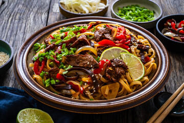 Asian style stir fried vegetables, roast beef and chow mein noodles on wooden table
