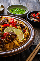 Asian style stir fried vegetables, roast beef and chow mein noodles on wooden table
