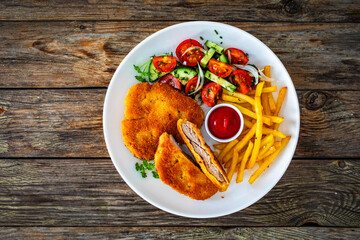 Crispy breaded fried pork loin chops with fries and fresh vegetables on wooden table
