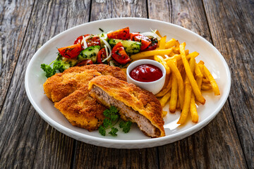 Crispy breaded fried pork loin chops with fries and fresh vegetables on wooden table
