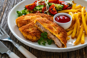 Crispy breaded fried pork loin chops with fries and fresh vegetables on wooden table
