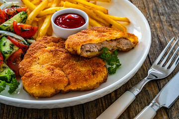 Crispy breaded fried pork loin chops with fries and fresh vegetables on wooden table
