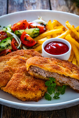 Crispy breaded fried pork loin chops with fries and fresh vegetables on wooden table
