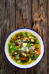 Pistou soup Nice - broth with basil pesto, bread, cheese and vegetables on wooden background in white bowl
