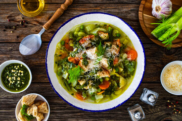 Pistou soup Nice - broth with basil pesto, bread, cheese and vegetables on wooden background in white bowl
