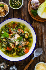 Pistou soup Nice - broth with basil pesto, bread, cheese and vegetables on wooden background in white bowl
