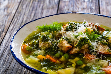 Pistou soup Nice - broth with basil pesto, bread, cheese and vegetables on wooden background in white bowl
