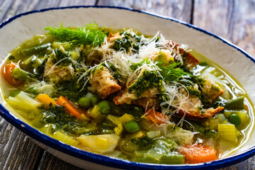 Pistou soup Nice - broth with basil pesto, bread, cheese and vegetables on wooden background in white bowl
