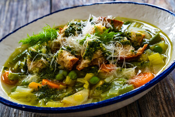 Pistou soup Nice - broth with basil pesto, bread, cheese and vegetables on wooden background in white bowl
