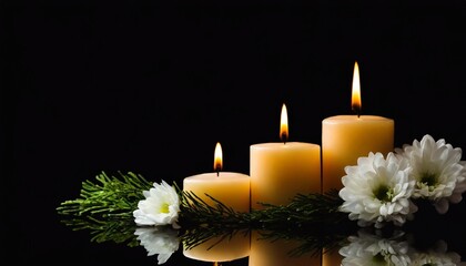 Burning candles with green branch and white flowers on black background.