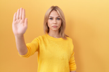 Young caucasian woman wearing yellow sweater doing stop sing with palm of the hand. warning expression with negative and serious gesture on the face.